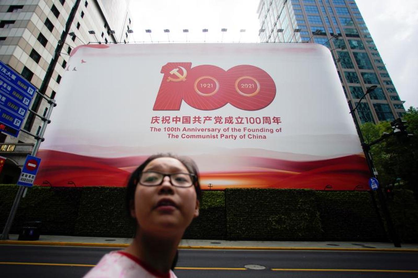 Una mujer camina en una calle frente a un letrero que marca el centenario de la fundación del Partido Comunista de China. 