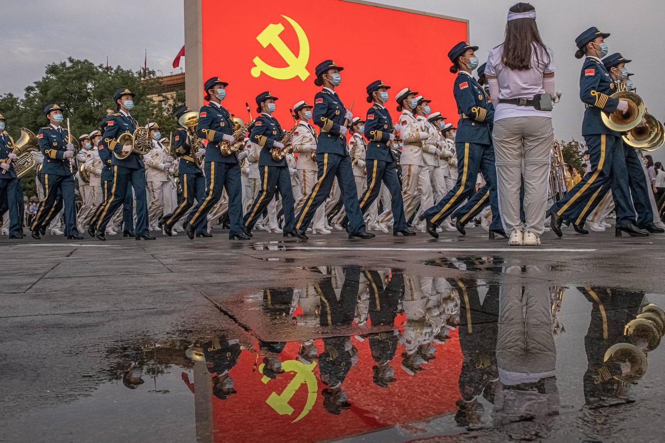 Miembros de la orquesta militar china desfilan frente a una pantalla que muestra la bandera comunista china. 