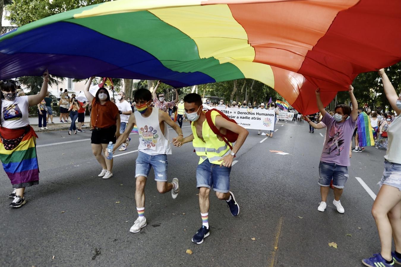 Dos jóvenes corren por debajo de una enorme bandera arcoíris. 