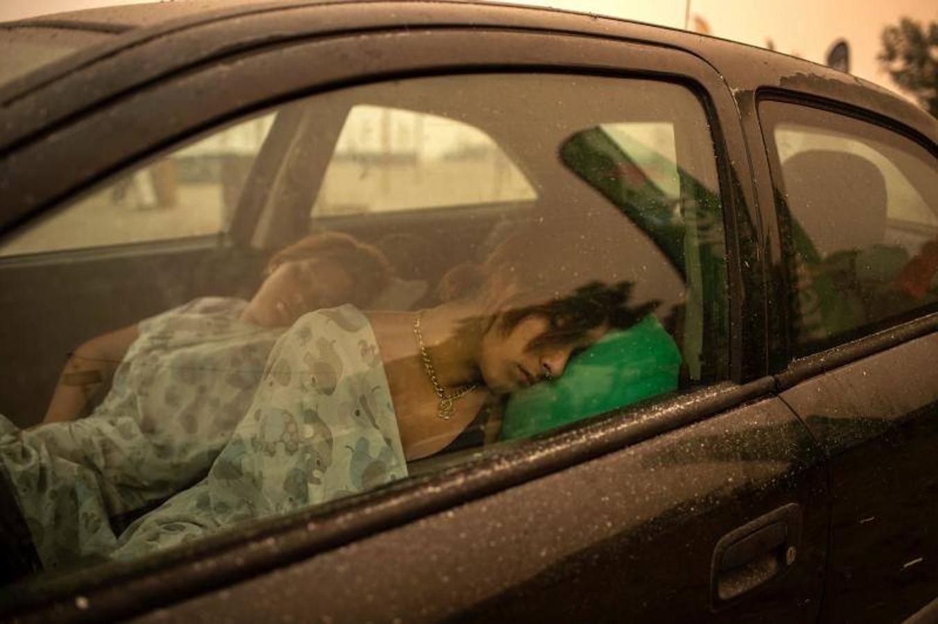 Una mujer duerme en su automóvil en la playa tras huir de las llamas. 
