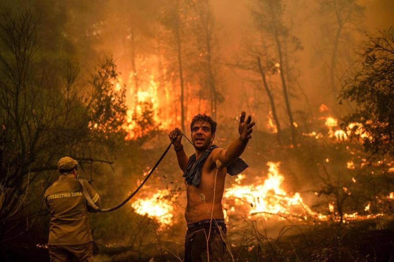 Un residente local hace un gesto mientras sostiene una manguera de agua vacía durante un intento de extinguir los incendios forestales que se acercan al pueblo de Pefki. 