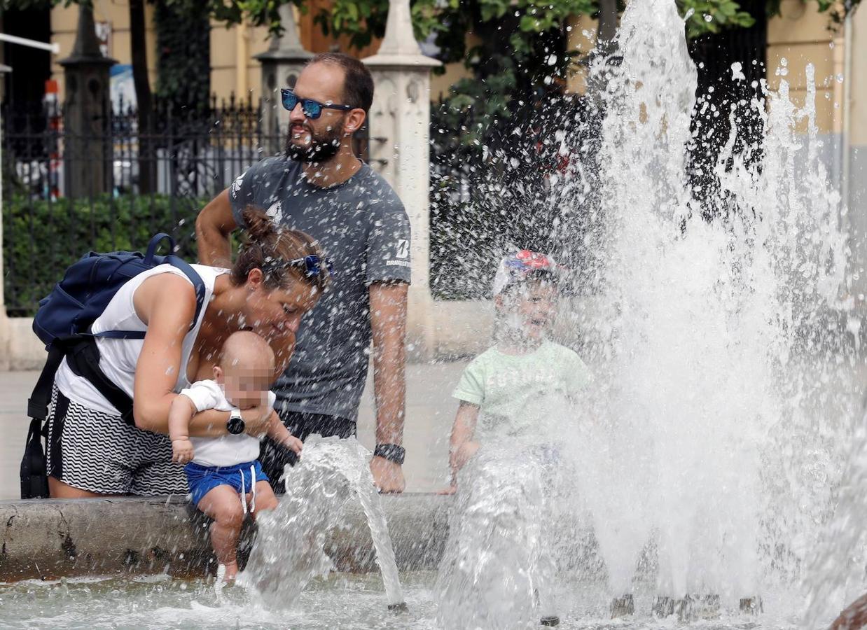 Varios ciudadanos se refrescan en una fuente de Valencia, donde se registrarán este sábado temperaturas en ascenso, significativamente altas tanto las mínimas como las máximas. 