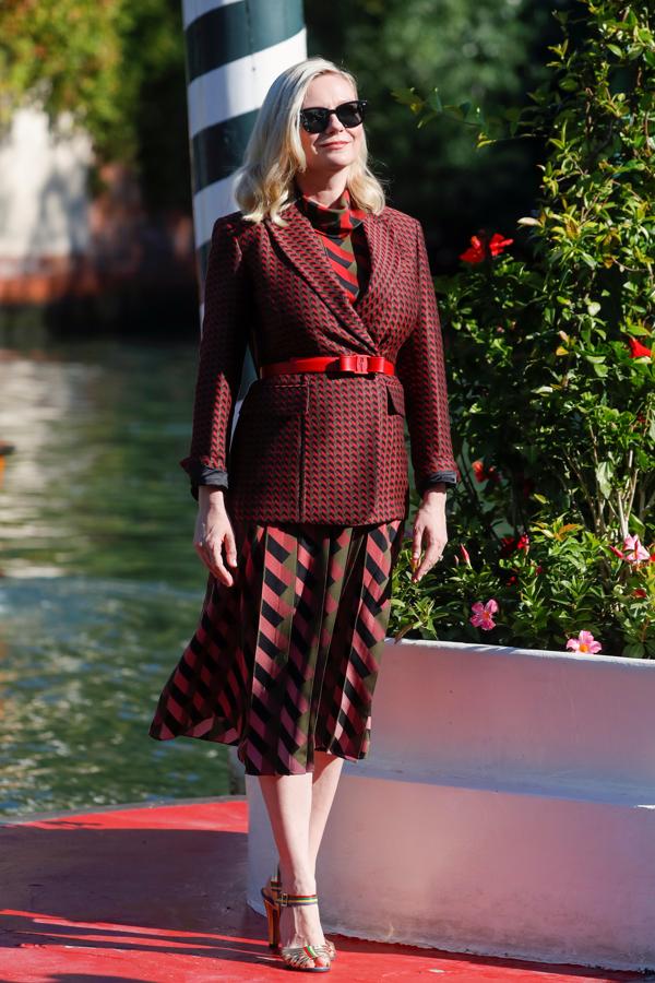 Kirsten Dunst, en el Festival de cine de Venecia 2021. La actriz lució un total look de Salvatore Ferragamo a su llegada al Festival. Su look estaba compuesto por un traje de chaqueta, falda con estampado geométrico y cinturón con cierre VIVA. Las sandalias forman parte de la línea `Creations' que recupera los diseños originales de la firma.