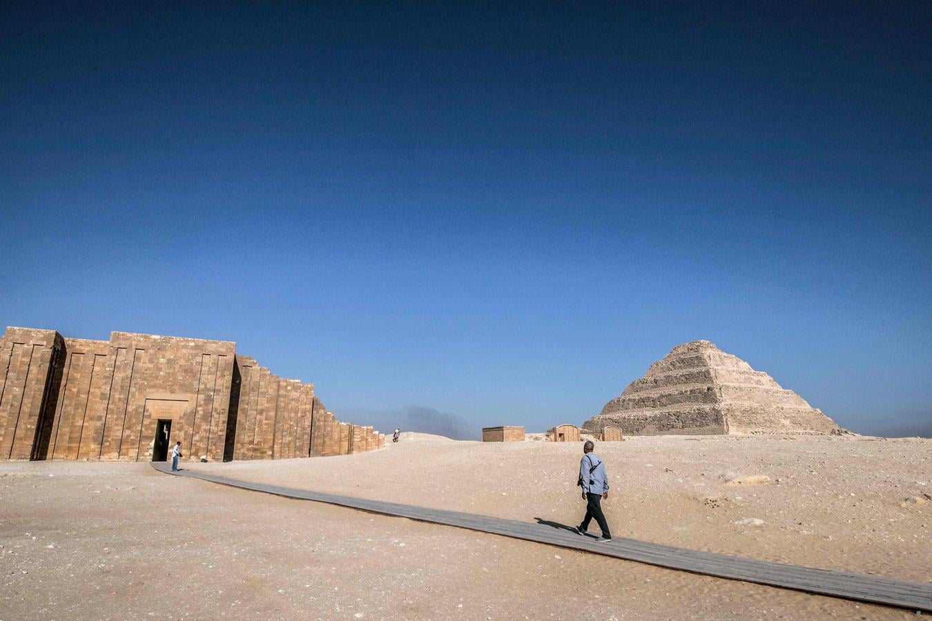 Un guardia de seguridad vestido de civil con un rifle de asalto camina cerca de la pirámide escalonada del faraón Zoser. 