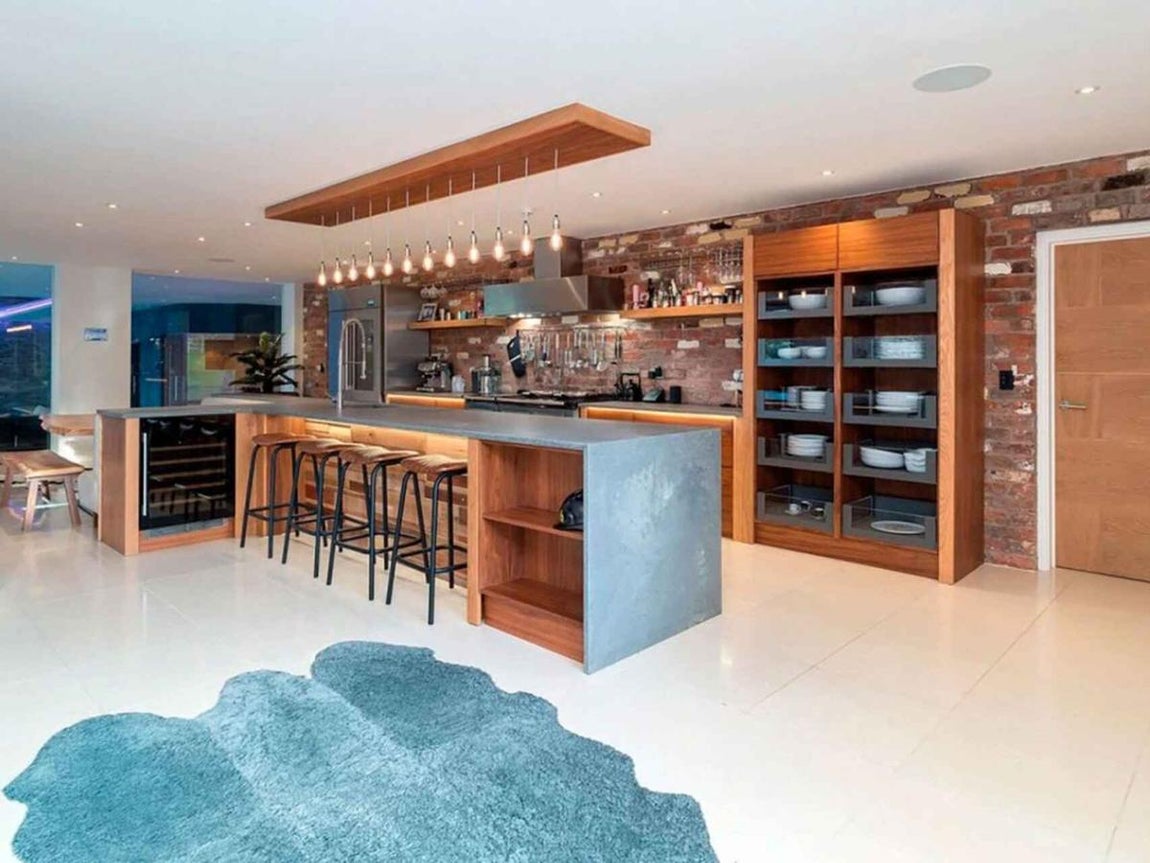 La nueva mansión de Cristiano en Mánchester. La cocina ofrece un aspecto más industrial, con la pared de ladrillo al descubierto y electrodomésticos en metal y madera. También está equipada con electrodomésticos de última generación y posee una isla central muy cómoda para desayunar o comer en ella.