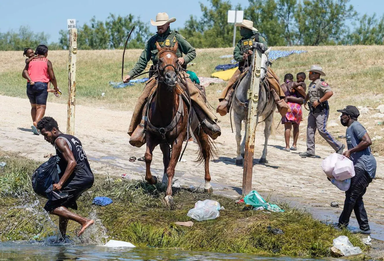 Dos agentes de la guardia fronteriza de EE.UU. usan las riendas de su caballo para evitar que varios migrantes haitianos ingresen al campamento. 