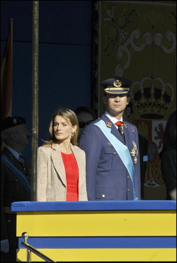 2006 - Los looks de la Reina Letizia en el Día de la Hispanidad. Aunque el rojo sea su tono favorito solo lo lució en 2006 con un vestido drapeado de Felipe Varela al que añadió un abrigo beige.