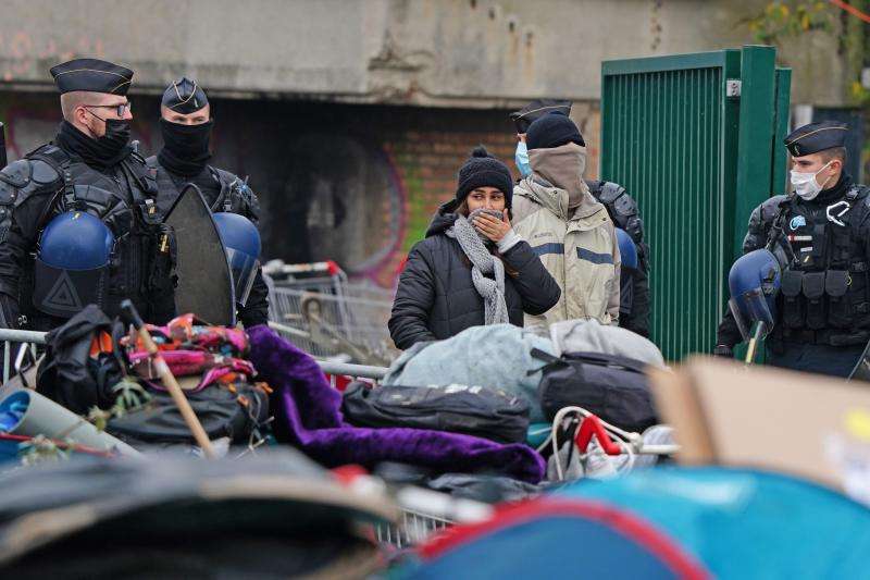 Varios inmigrantes se protegen del frío durante el desalojo, vigilados por los agentes. 