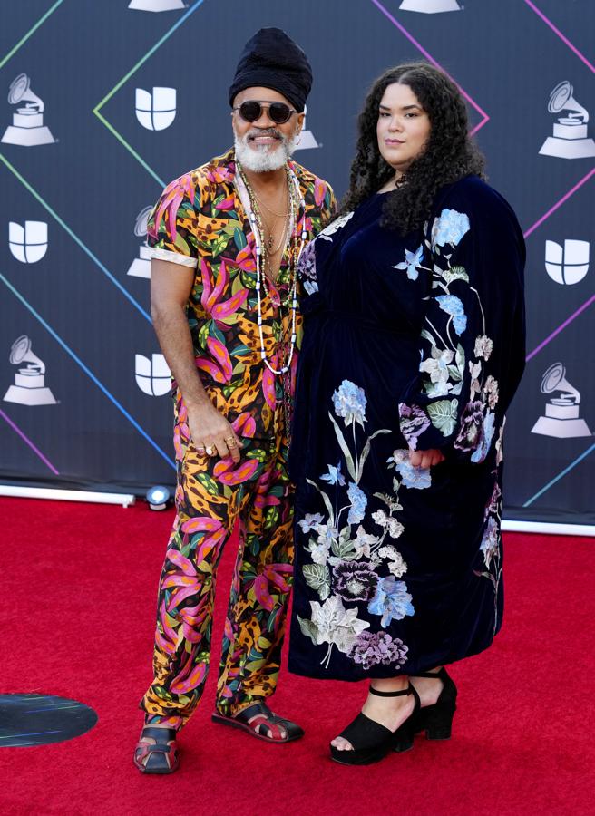 Carlinhos Brown y Nina de Freitas - Alfombra roja de los Grammy Latinos 2021. Muy colorido con un traje de aires tropicales con estampados florales y animal print. Añadió un pañuelo negro y collares XXL para rematar el look.