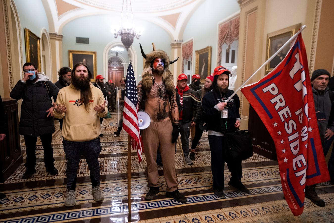 Un hombre disfrazado de bisonte y autoproclamado «chamán de QAnon» asalta el Capitolio acompañado de otras personas con gorras y banderas en apoyo al entonces presidente de Estados Unidos, Donald Trump. 