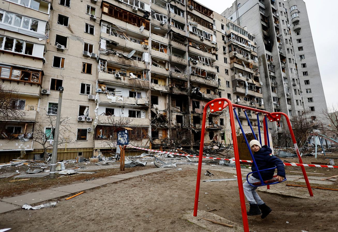 Un niño se columpia frente a un edificio destruido. 