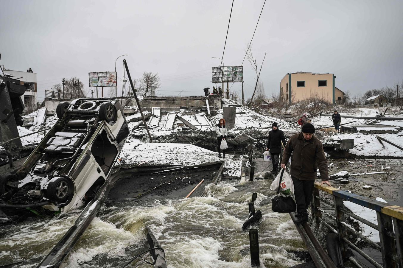 Muchas infraestructuras están ya dañadas por los ataques rusos. En la imagen, varios civiles cruzan un río en un puente volado en el frente norte de Kiev. 