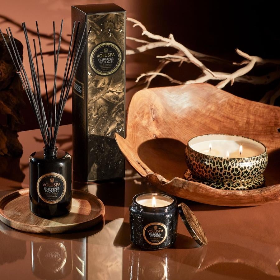 Voluspa - Regalos para acertar en el Día del Padre. Pack de velas en lata Burning Woods con aroma a madera cortada de abeto y enebro del Himalaya, de Voluspa. Está disponible en seis formatos, que se presentan acompañados de lujosos frascos en tonos negro perlado, cobre y detalles metálicos dorados, sobre los que se dibujan elegantes estampados y texturas en relieve inspirados en los mosaicos árabes del siglo VIII. Precio: 90€.