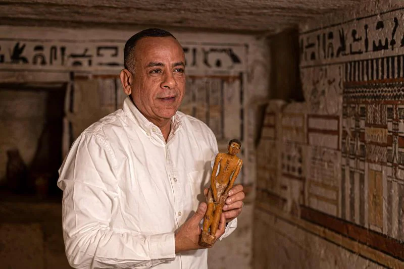 Mostafa Waziri, secretario general del Consejo Supremo de Antigüedades de Egipto, sostiene una pequeña estatuilla el 19 de marzo de 2022, dentro de una de las cinco antiguas tumbas faraónicas descubiertas en el sitio arqueológico de Saqqara, al sur de la capital. (Foto: AFP)