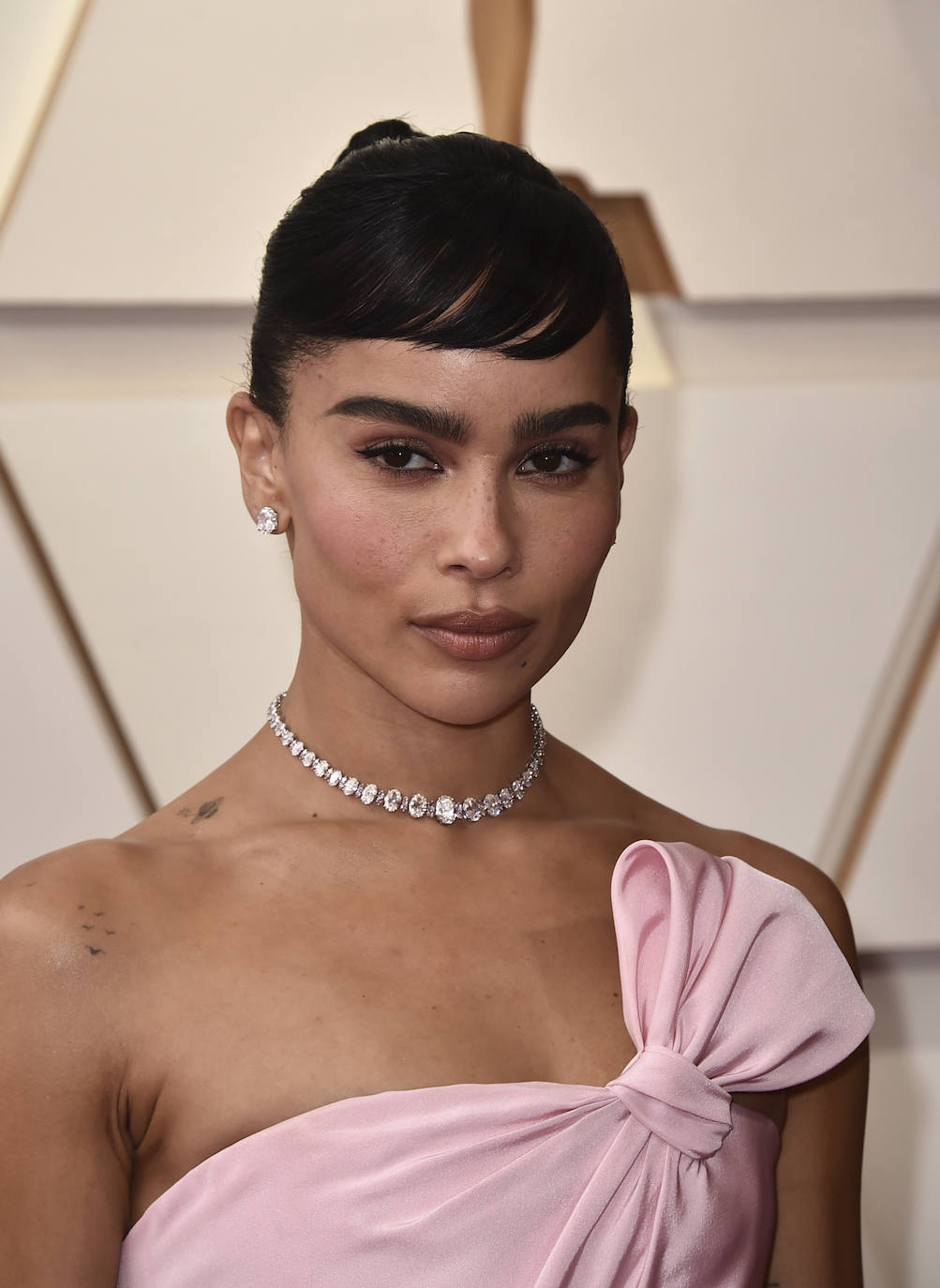 Zoe Kravitz ha lucido un bonito look beauty en los Oscar 2022. La actriz ha apostado por un moño de bailarina con flequillo  corto, que recuerda al mítico de Audrey Hepburn. En cuanto al maquillaje, destaca su eyeliner, un discreto cat eye, y sus sombras, pómulos y labios en color rosa, a juego con el vestido.