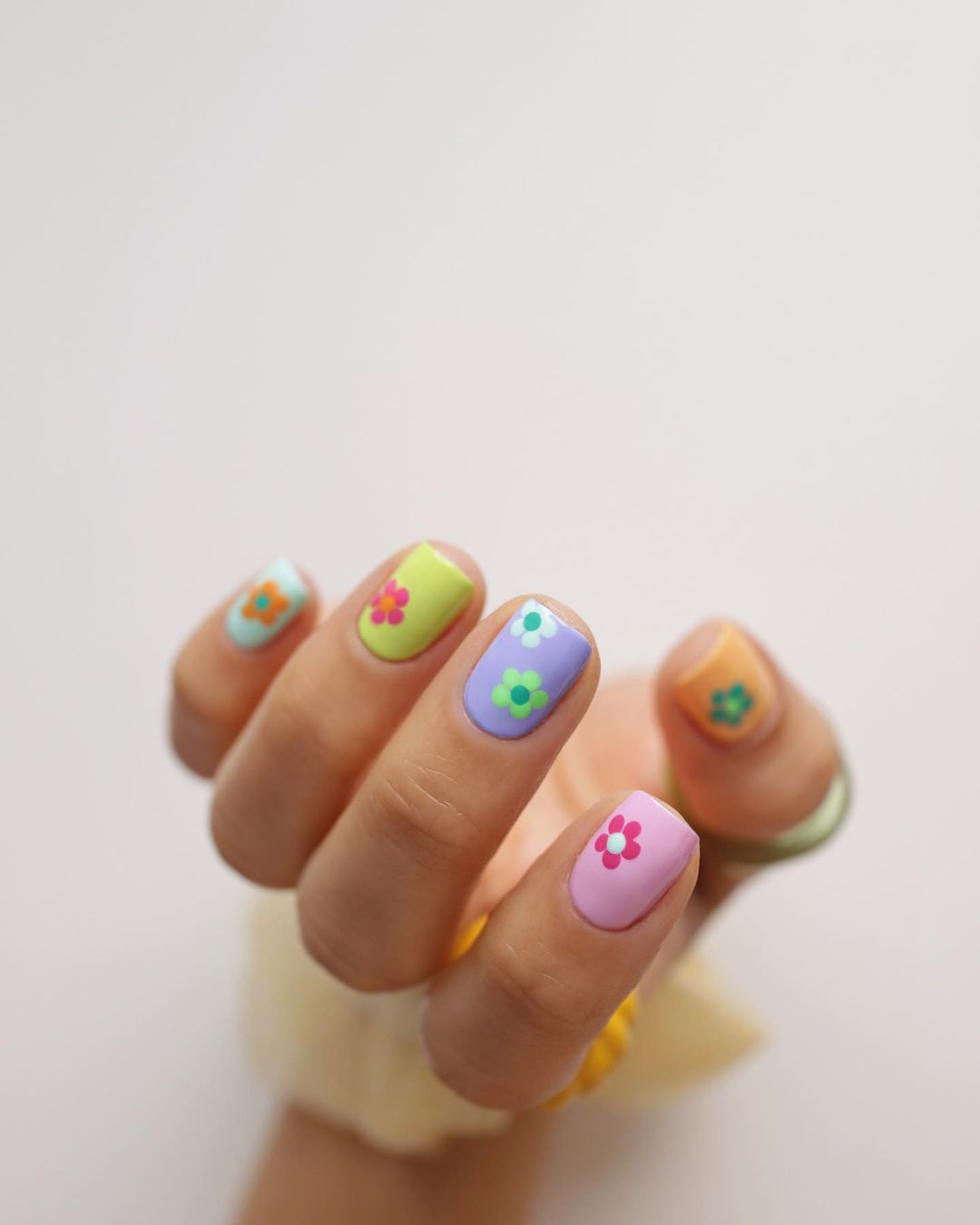 Manicura multicolor y flores en uñas cortas. En las uñas cortas también se pueden llevar manicuras originales como esta que combina la tendencia multicolor en tonos pastel con los dibujos de flores. (Instagram @thehangedit).