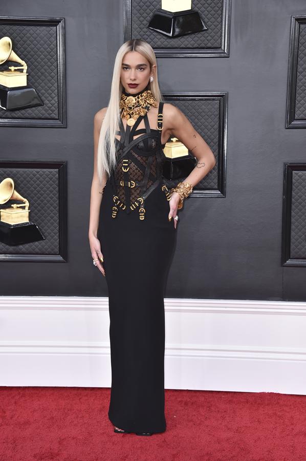 Dua Lipa - Alfombra roja de los Grammy 2022. Rescató una de las tendencias más icónicas de Donatella Versace a principios de los noventa, los vestidos con correas que popularizaron modelos como Cindy Crawford.  Un diseño muy dramático al que añadió un gran colgante y pulseras a juego que potenciaba el resultado.