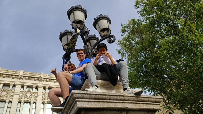 Tres seguidores encaramados a una farola en la calle de Alcalá