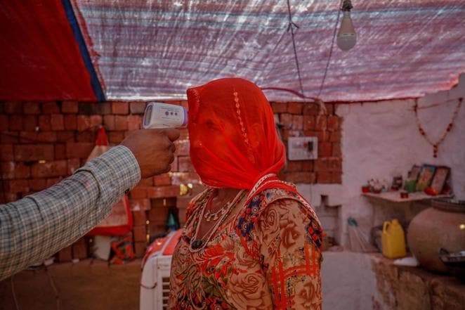 Un sanitario comprueba la temperatura de una mujer dentro de su choza durante una campaña de vacunación para trabajadores de una fábrica de ladrillos en la aldea de Kavitha, en las afueras de Ahmedabad, el 8 de abril de 2021