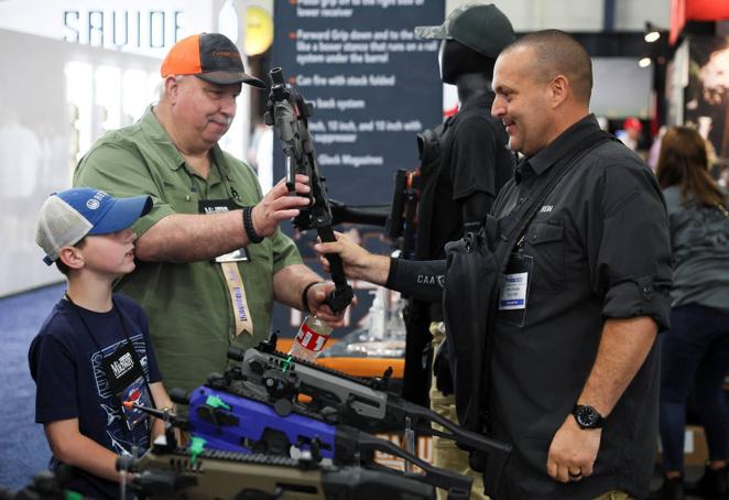 Un hombre sostiene un kit de conversión de pistola junto a un niño en la Convención Nacional del Rifle celebrada en Houston (Texas).