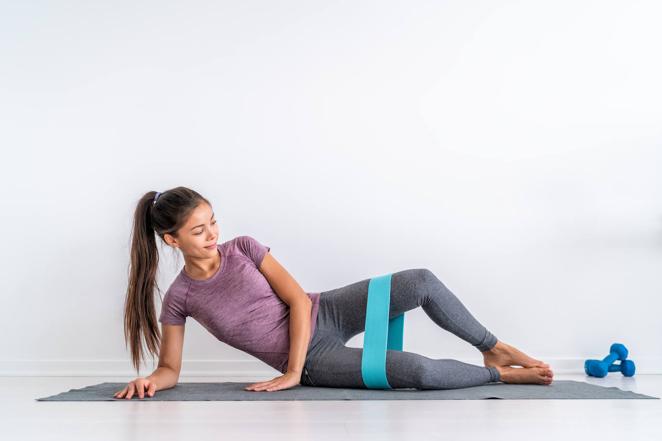 Abducción de cadera. Tumbado también sobre un lateral, mantén la cadera apoyada en el suelo y apóyate sobre el antebrazo. Flexiona las rodillas, junta los pies y, con la banda colocada por encima de las rodillas, abre y cierra las piernas hasta donde te permita la cinta. Es importante que contraigas el glúteo cuando abras las piernas. Con este ejercicio trabajarás sobre todo abductores y glúteo medio.