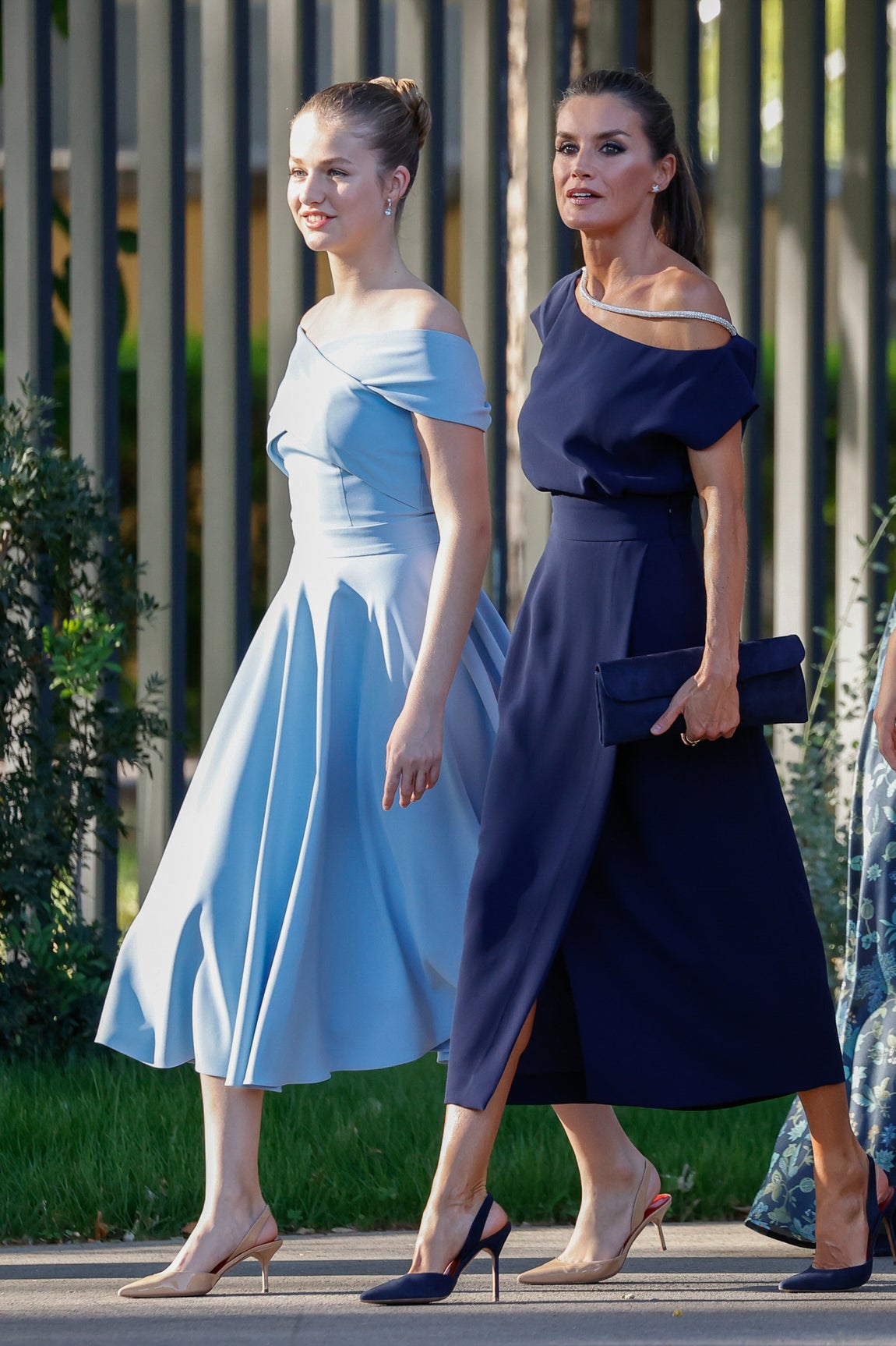 Madre e hija. Doña Letizia y Leonor en absoluta sintonía de estilo: vestidos de largo medio, azules ambos y los dos con escote similar, que dejaba hombros a la vista. El de la madre, en un tono más oscuro, el de la hija en un jovial color cielo. La primera, con un hombro al descuberto y detalle de brillos; la segunda, con escote cruzado sobre el pecho, estilo barco. Ambas, con el pelo recogido y con zapatos tipo salón destalonados.