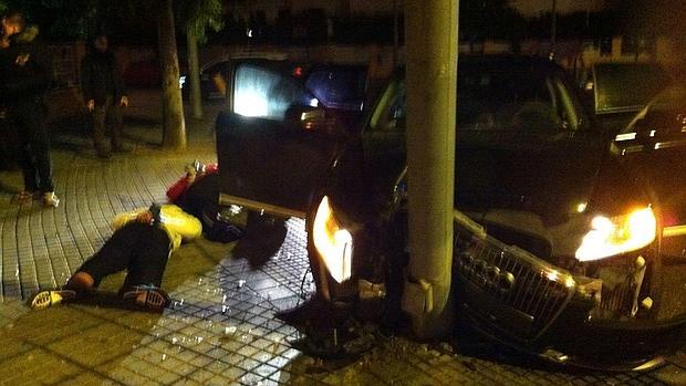 Aspecto del coche empotrado en una farola y dos de los detenidos en el suelo