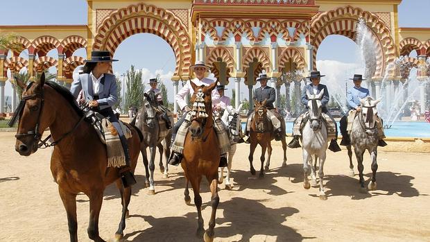 Un grupo de amazonas y jinetes frente a la portada de la Feria de Córdoba