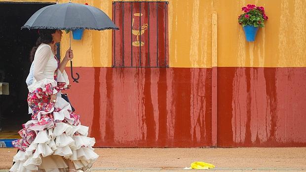 Una joven vestida de gitana camina bajo un paraguas por la Feria de Córdoba