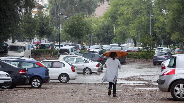 Una mujer atraviesa el solar, inundado por las lluvias, entre los coches aparcados