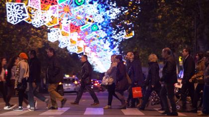 Algunas personas cruzan un paso de peatones en una calle adornada con luces de Navidad