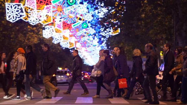 Algunas personas cruzan un paso de peatones en una calle adornada con luces de Navidad