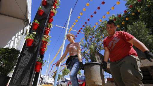 Dos personas entran con una maceta en una caseta de la Feria