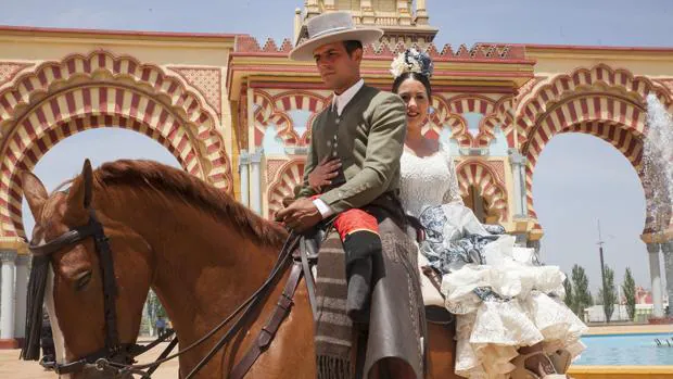 Una pareja a lomos de un caballo frente a la portada de la Feria de Córdoba