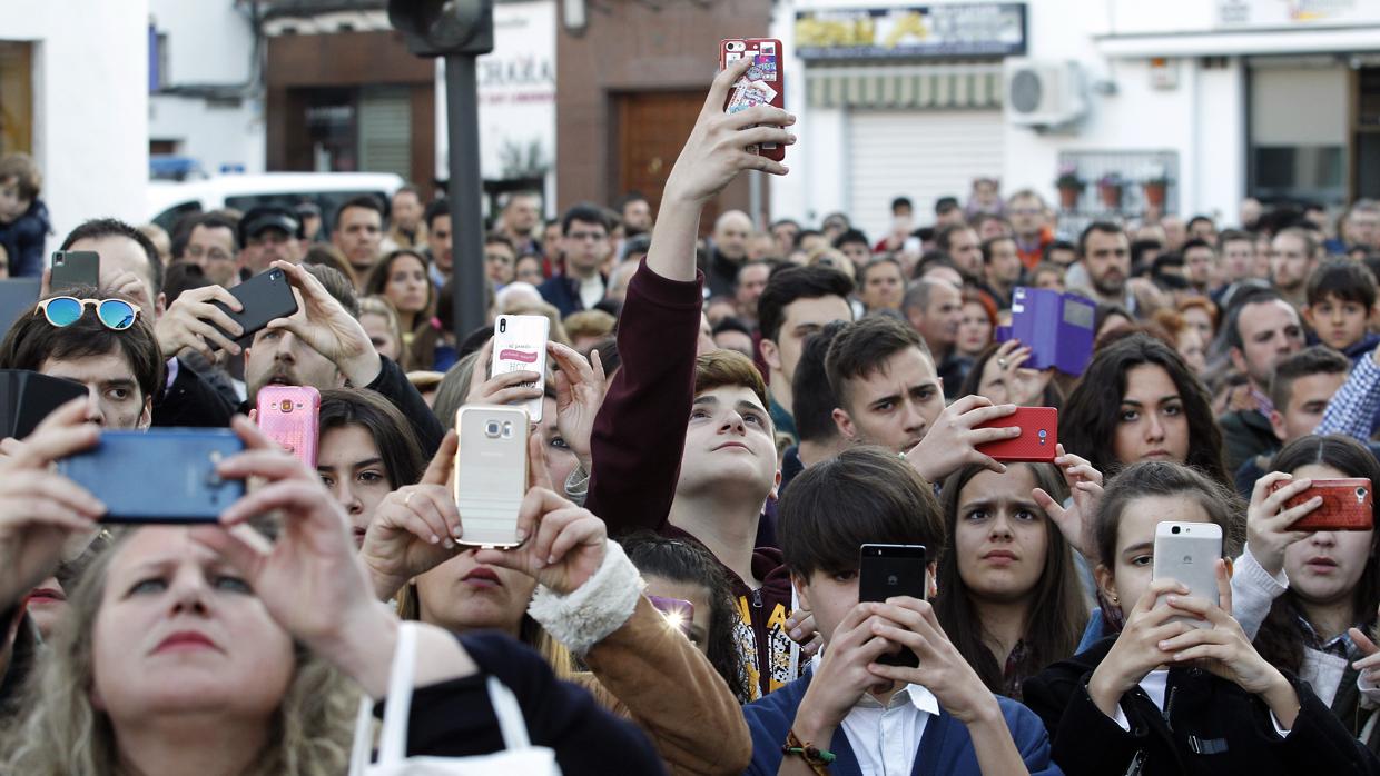 Unas personas toman fotografías al paso de una hermandad