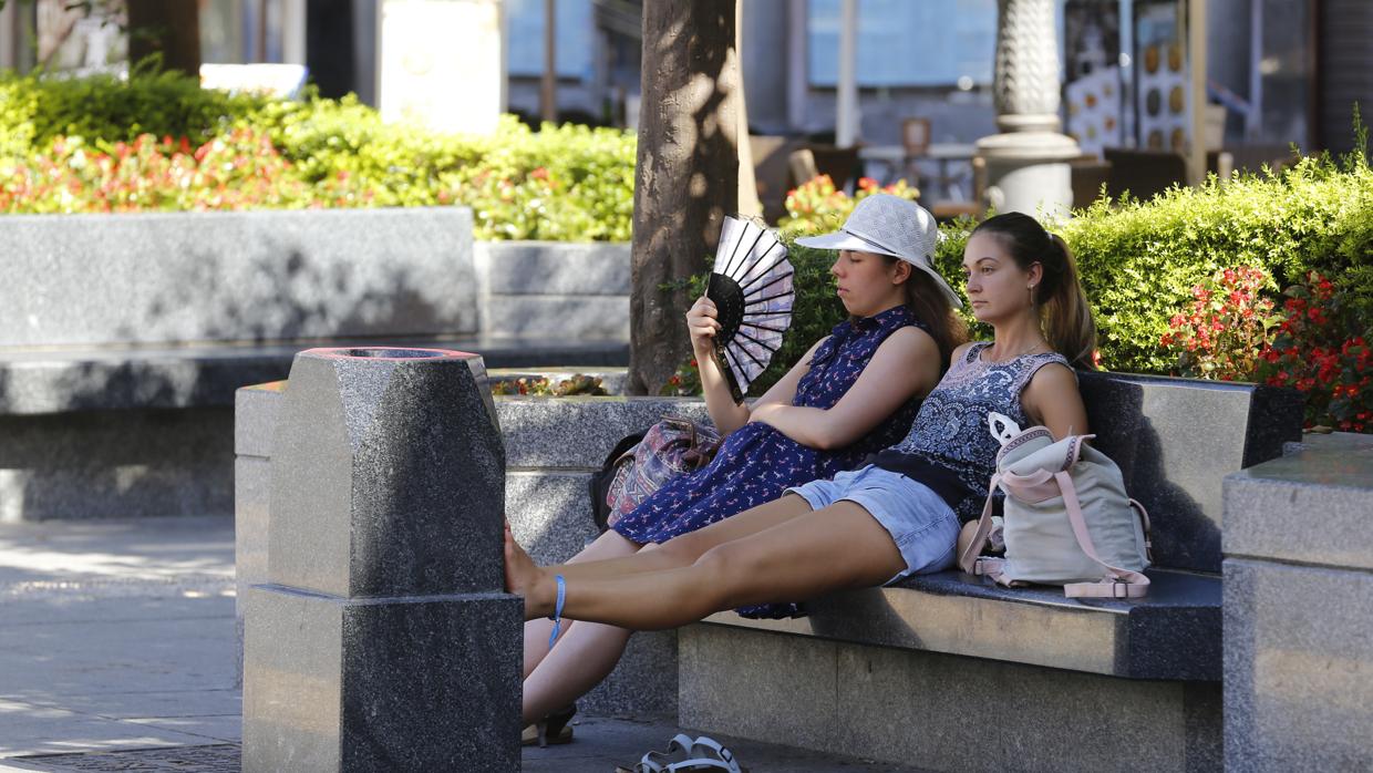 Dos personas se refugian del calor a la sombra en la Plaza de las Tendillas