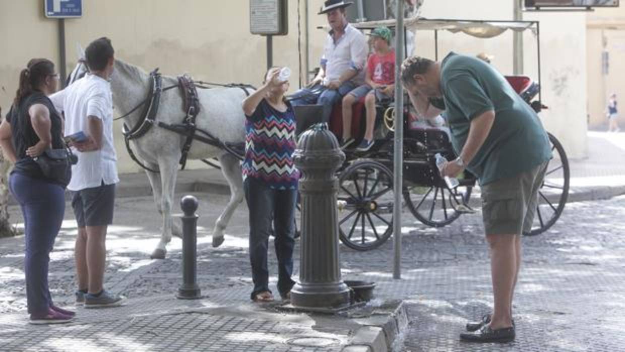 Dos personas se refrescan en una fuente en Campo Santo de los Mártires