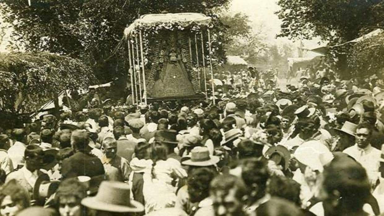 Procesión de la Virgen en 1915 en una aldea con chozas y llevando una ráfaga del siglo XIX