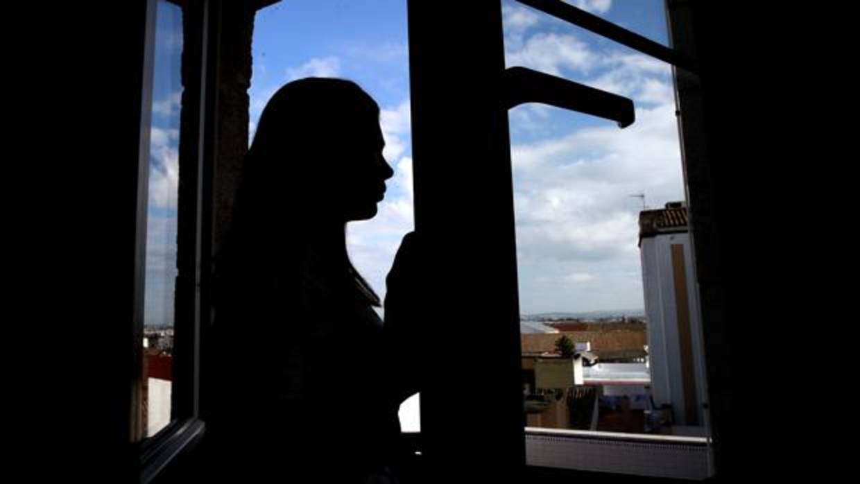 Una adolescente mira por la ventana de su vivienda en Córdoba al contraluz