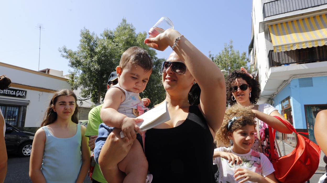 Una madre refresca a su hijo con agua a la salida del colegio