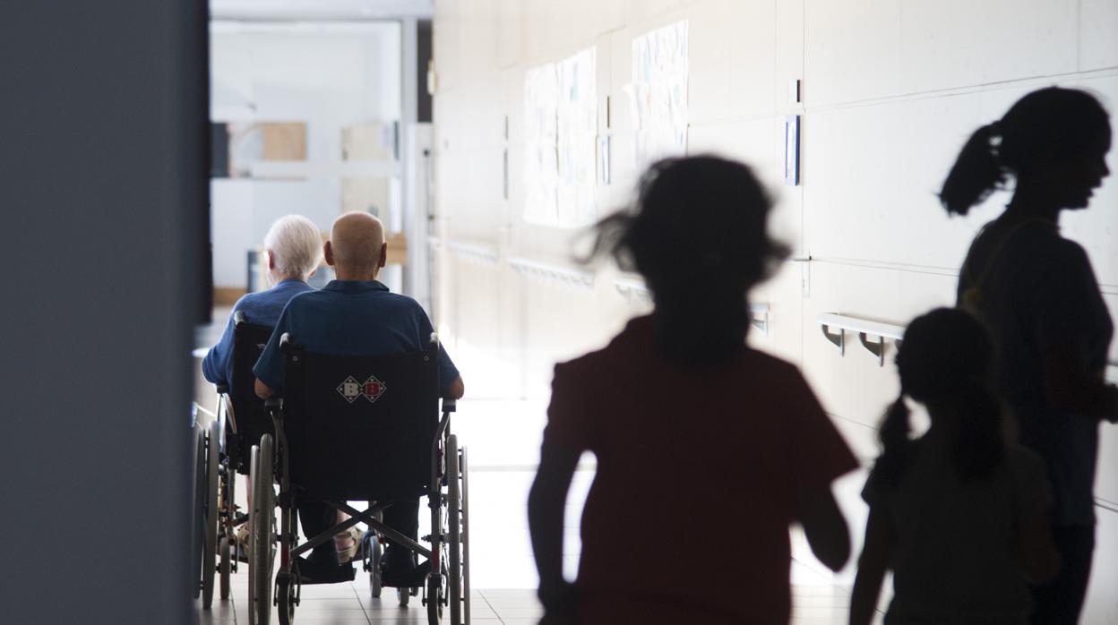 Dos ancianos seguidos de niños, en sillas de ruedas