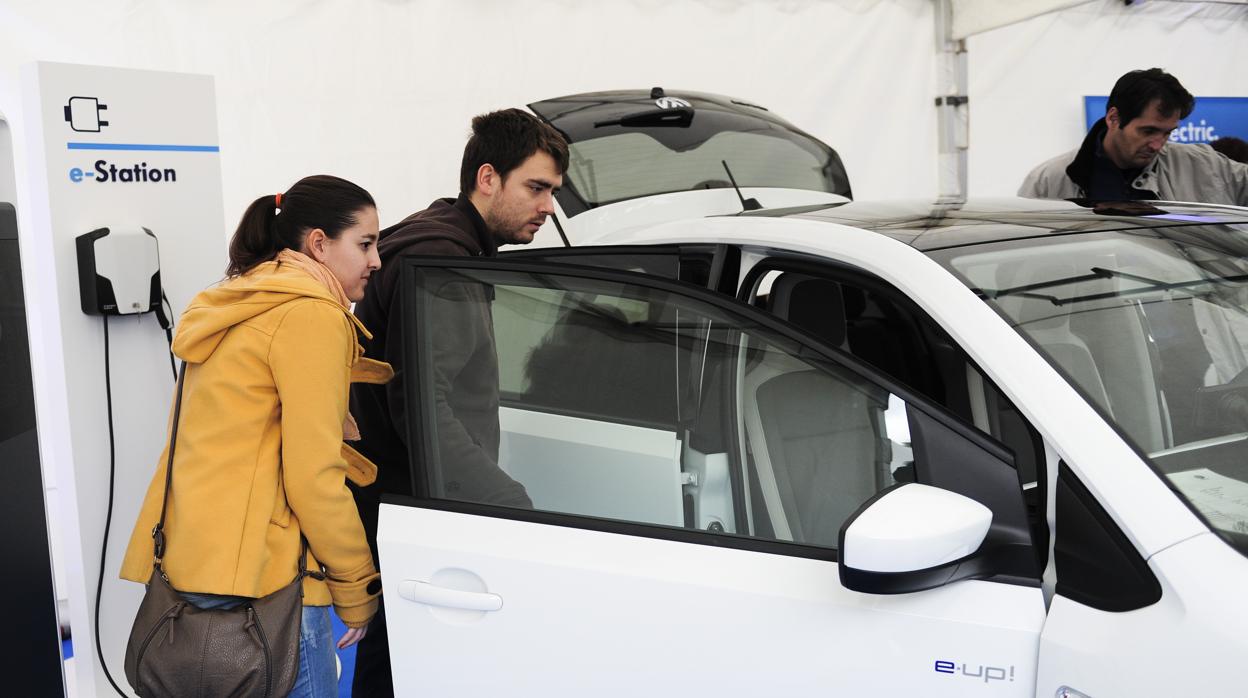 Dos personas observan en un concesionario un coche eléctrico, junto a un punto de recarga