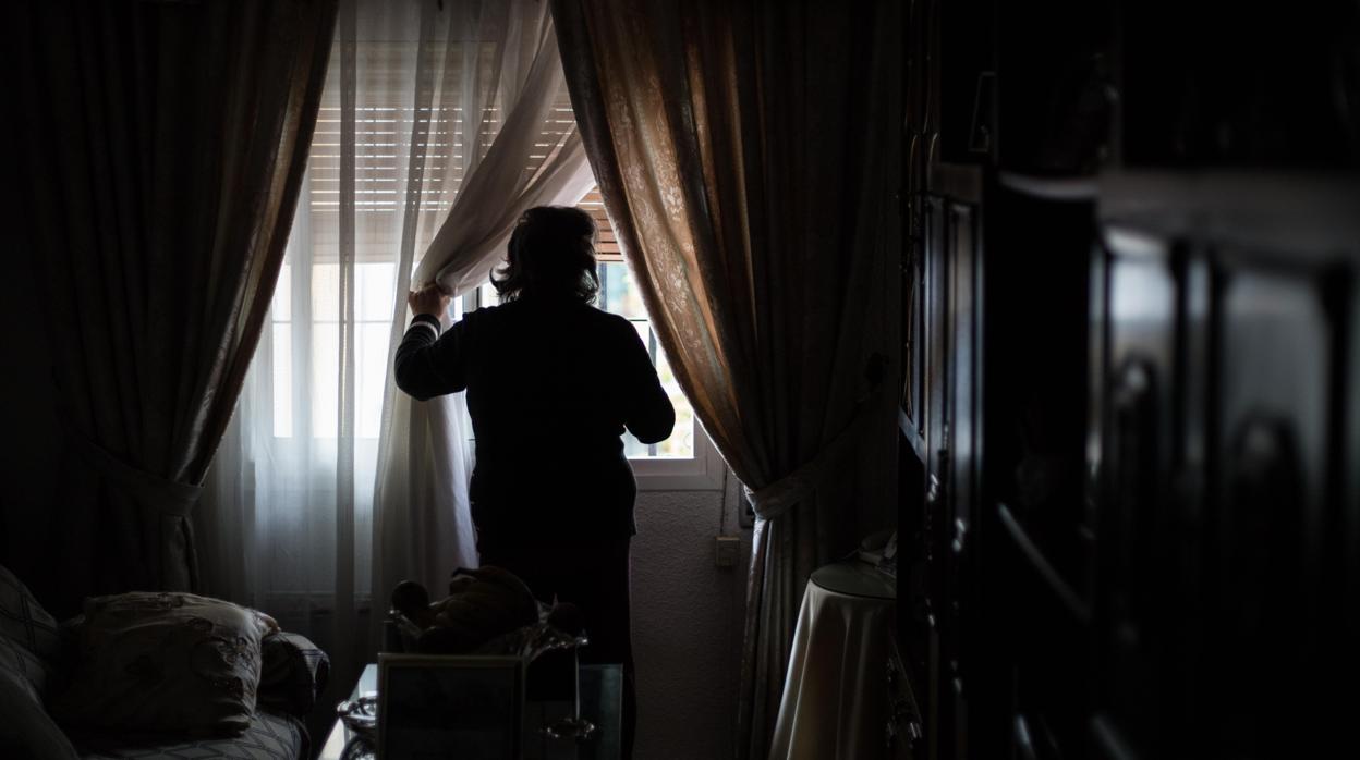 Una mujer de avanzada edad mira a través de la ventana de su vivienda