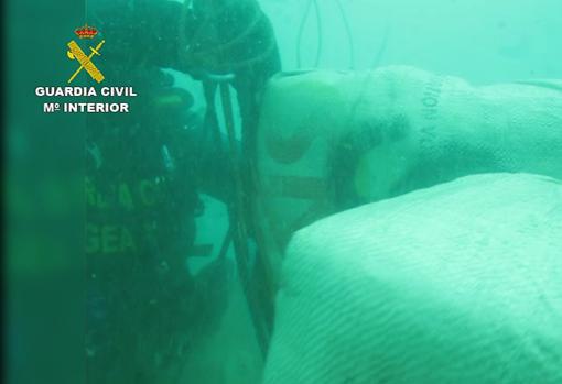 Imagen tomada bajo el mar en la que los agentes recuperan varios fardos de hachís.