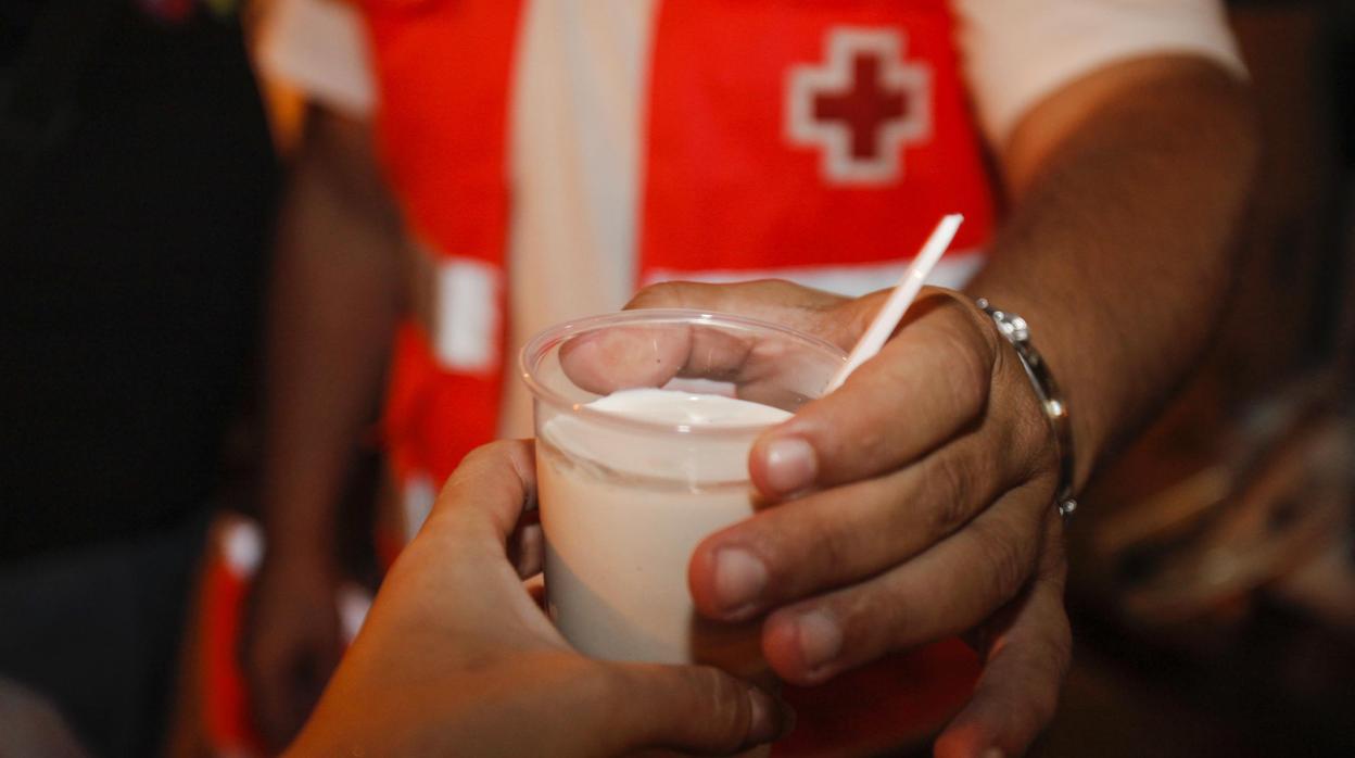 Un voluntario de Cruz Roja tiende un vaso de leche a un usuario