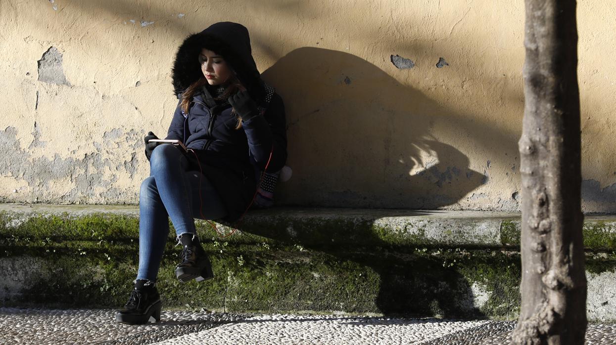 Una joven consulta su teléfono móvil al sol en un frío día de invierno