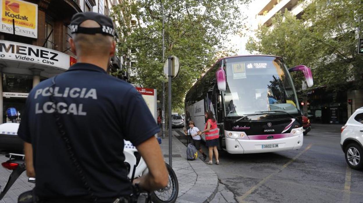 Un agente local vigila un autobús escolar en Ronda de los Tejares en el primer día del curso de este año