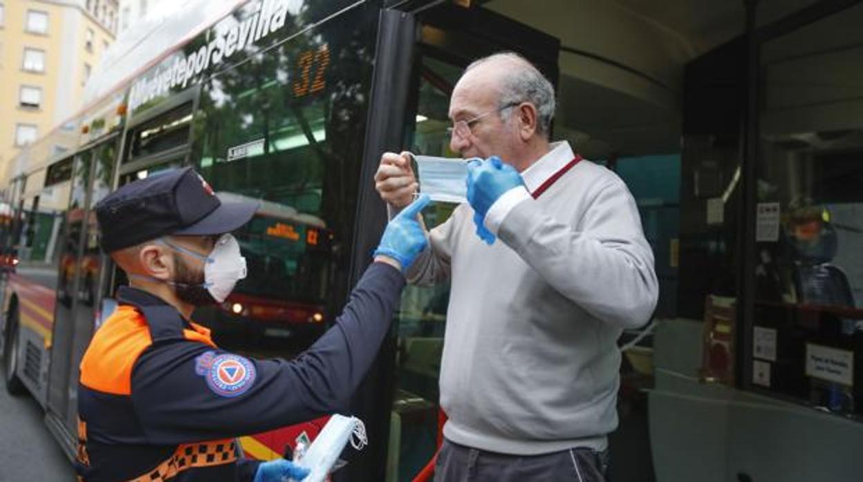 Un agente de Protección Civil reparte mascarillas a un usuario de autobús