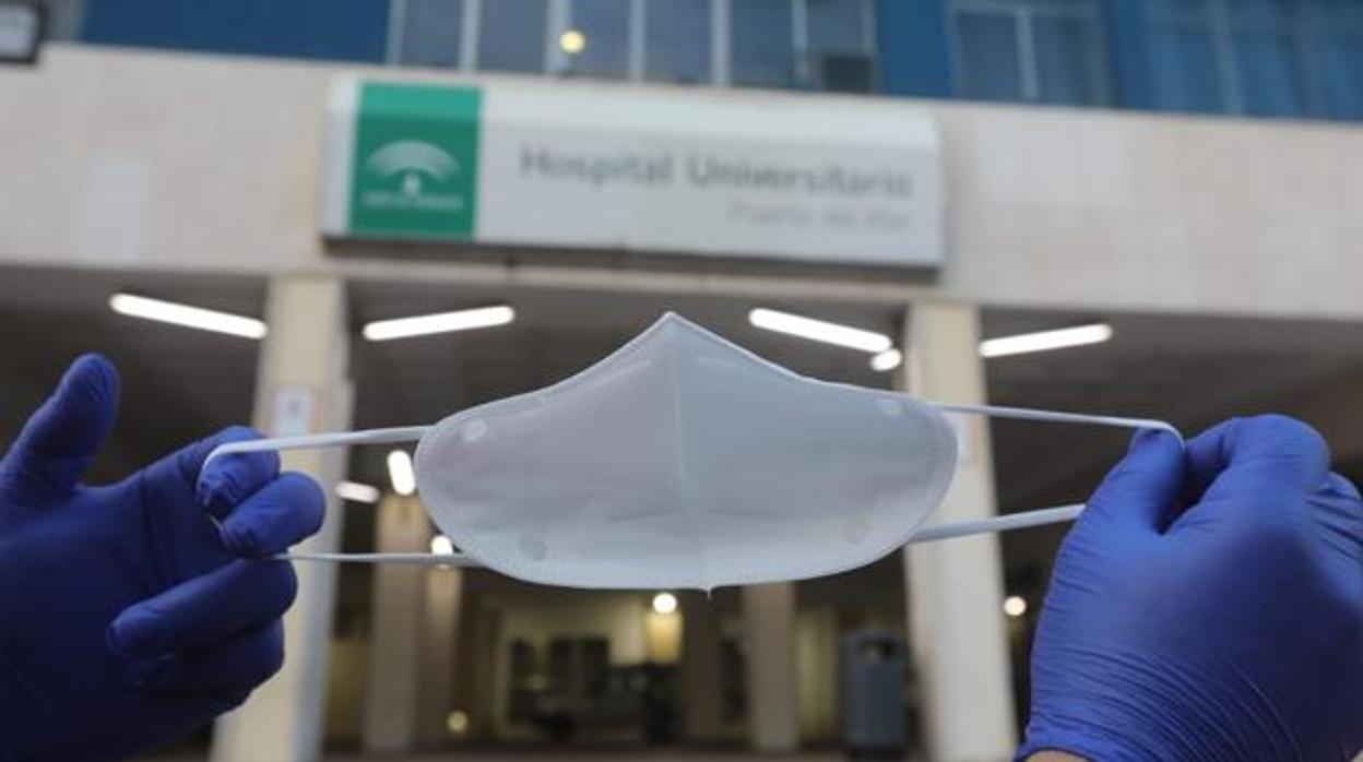 Sanitario posa con una mascarilla en la mano a la puerta de un hospital