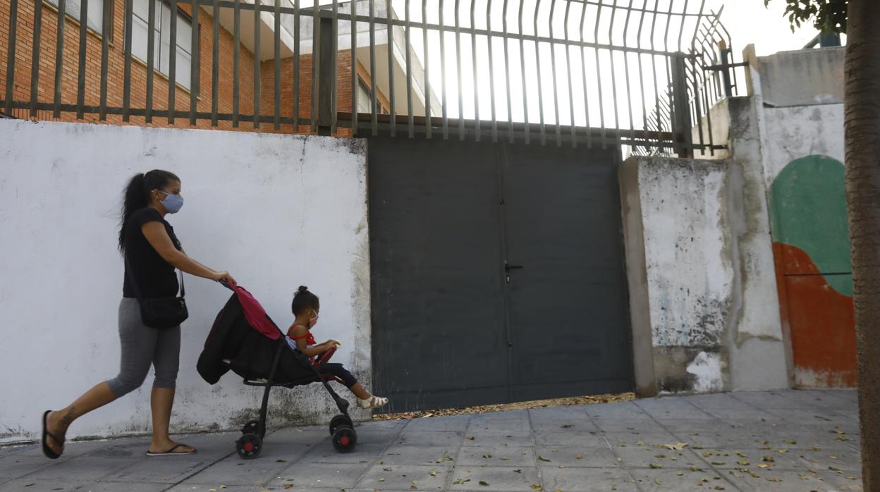 Una mujer con una niña en un carrito en la puerta de un centro escolar de Córdoba